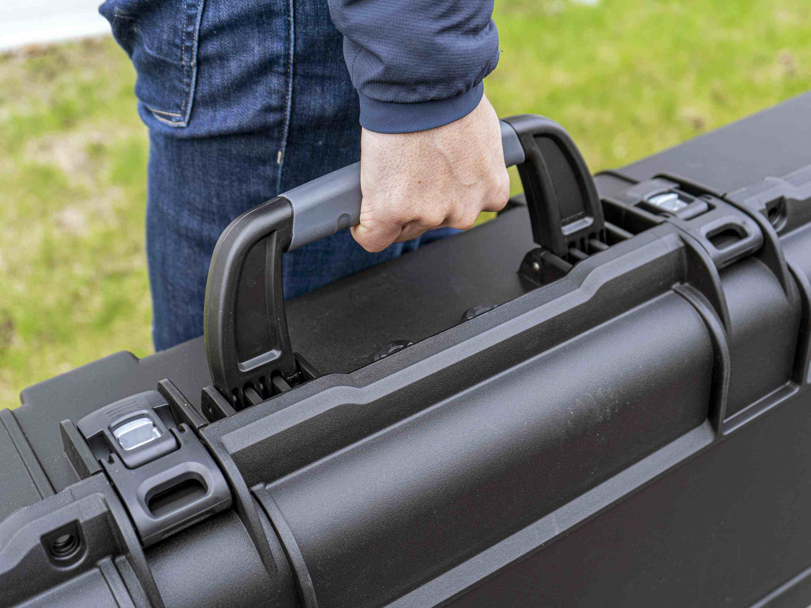 Person holding a black hard-shell suitcase outdoors