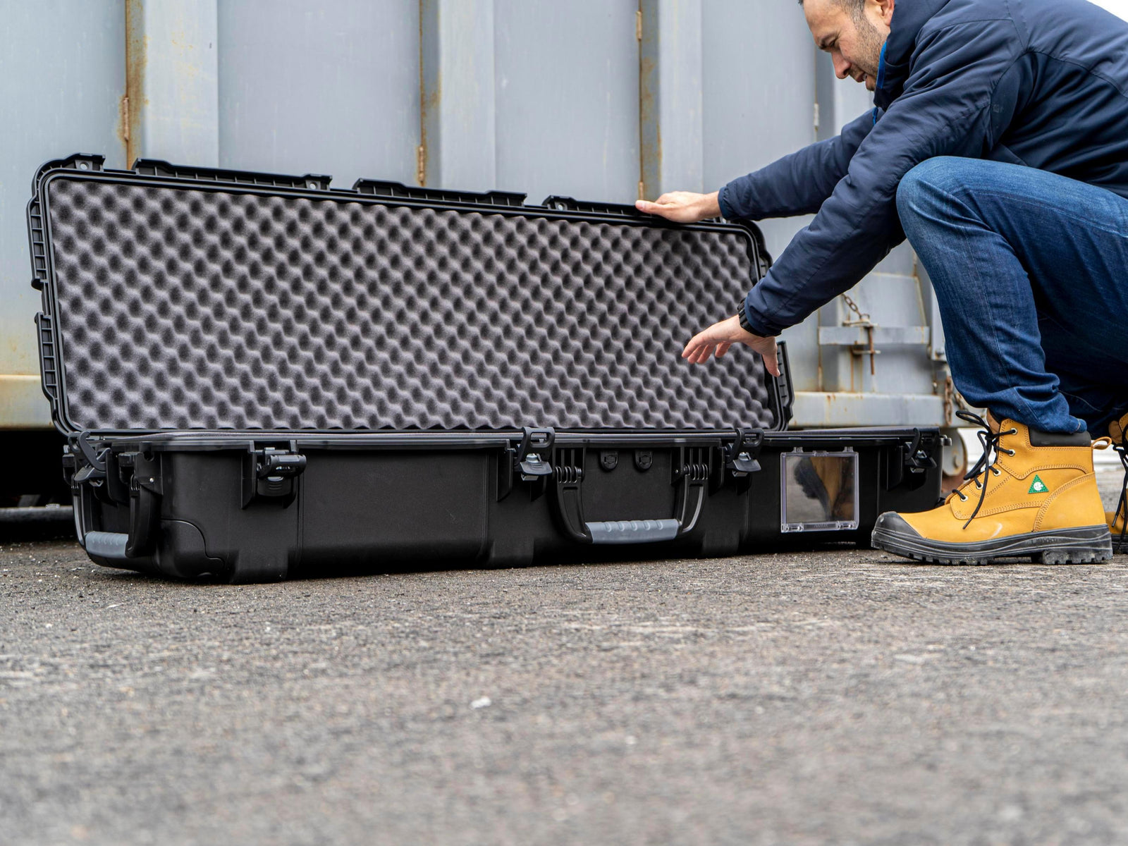 Person opening a large black and gray foam-lined case outdoors.