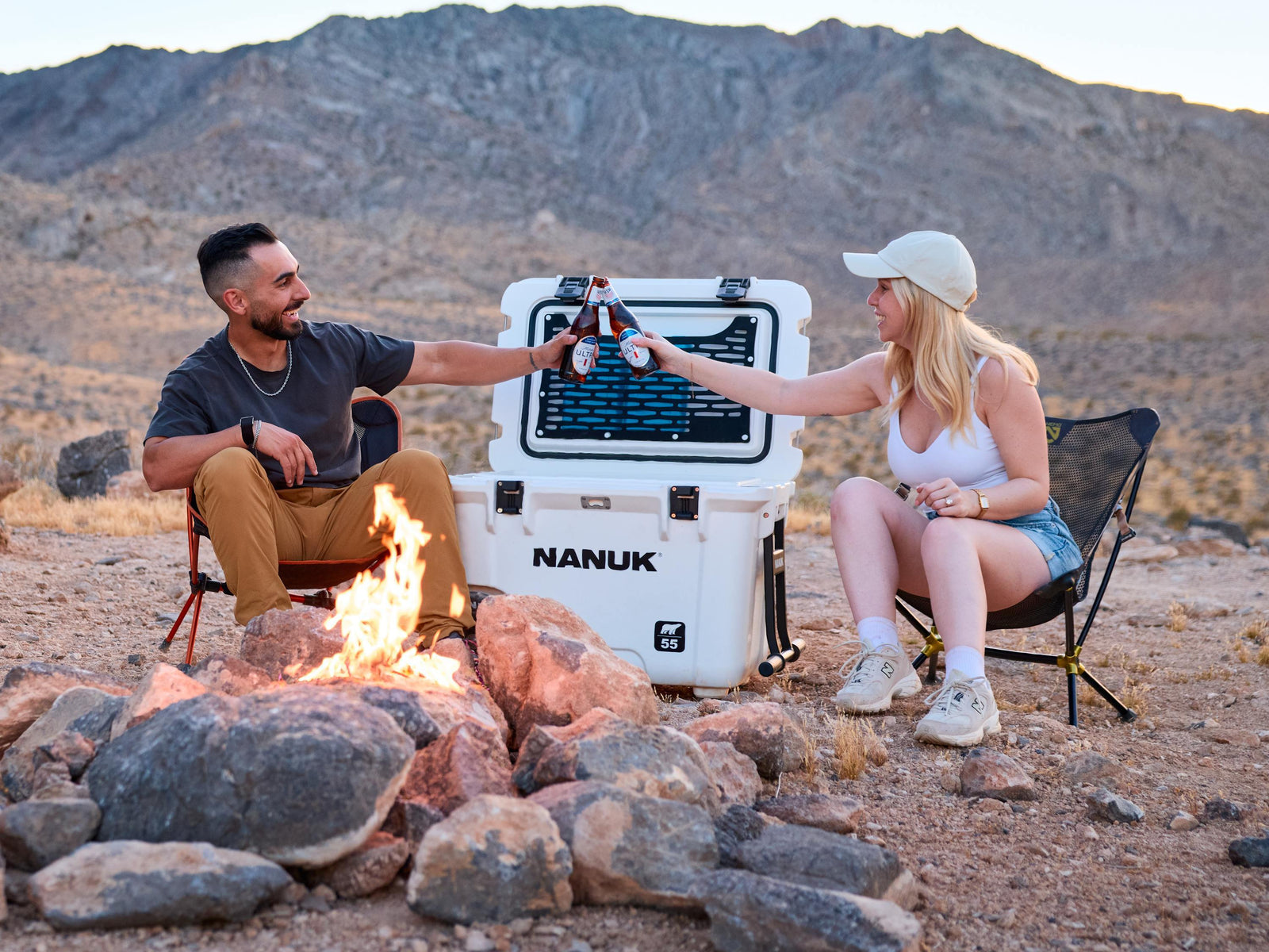 Two people sitting by a campfire with a NANUK cooler in the desert.