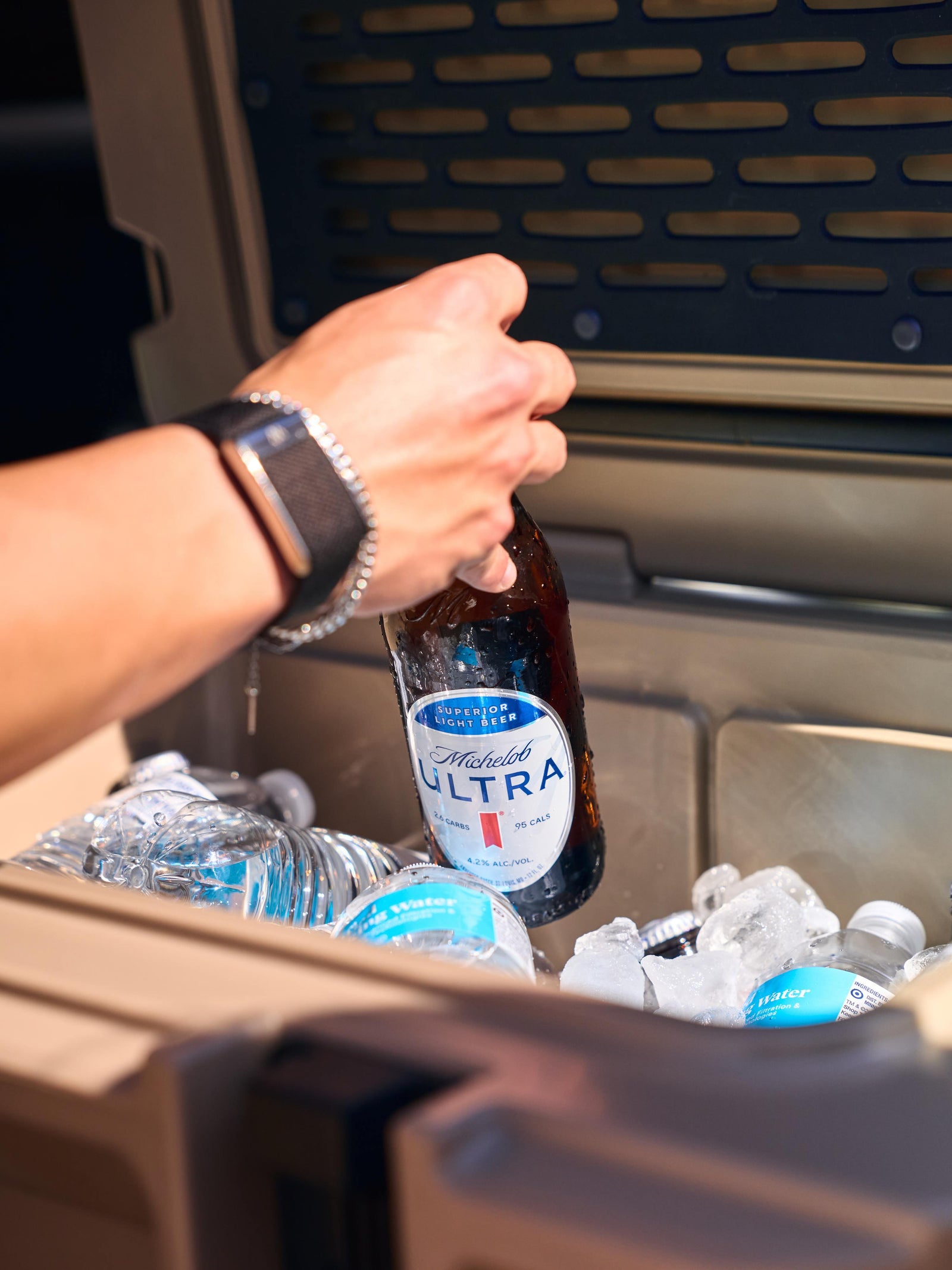 Person placing a bottle of Michelob Ultra in a cooler with ice and water bottles.