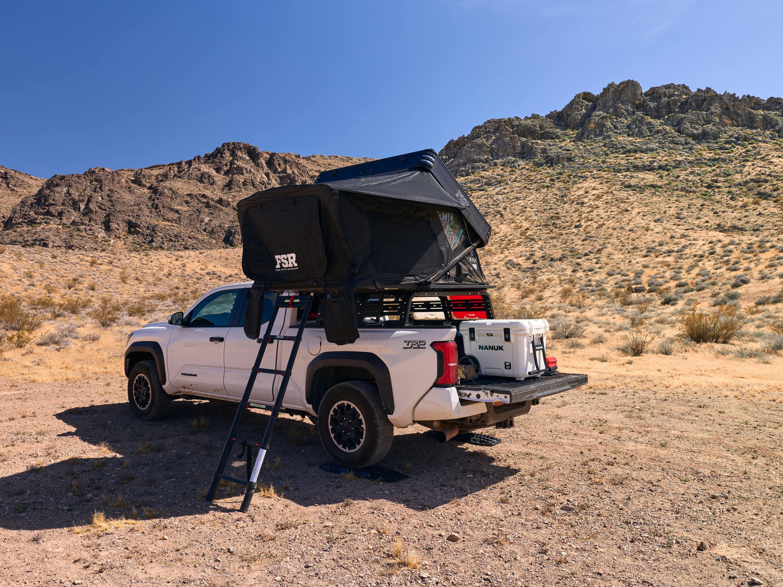 White truck with a black rooftop tent in a desert landscape
