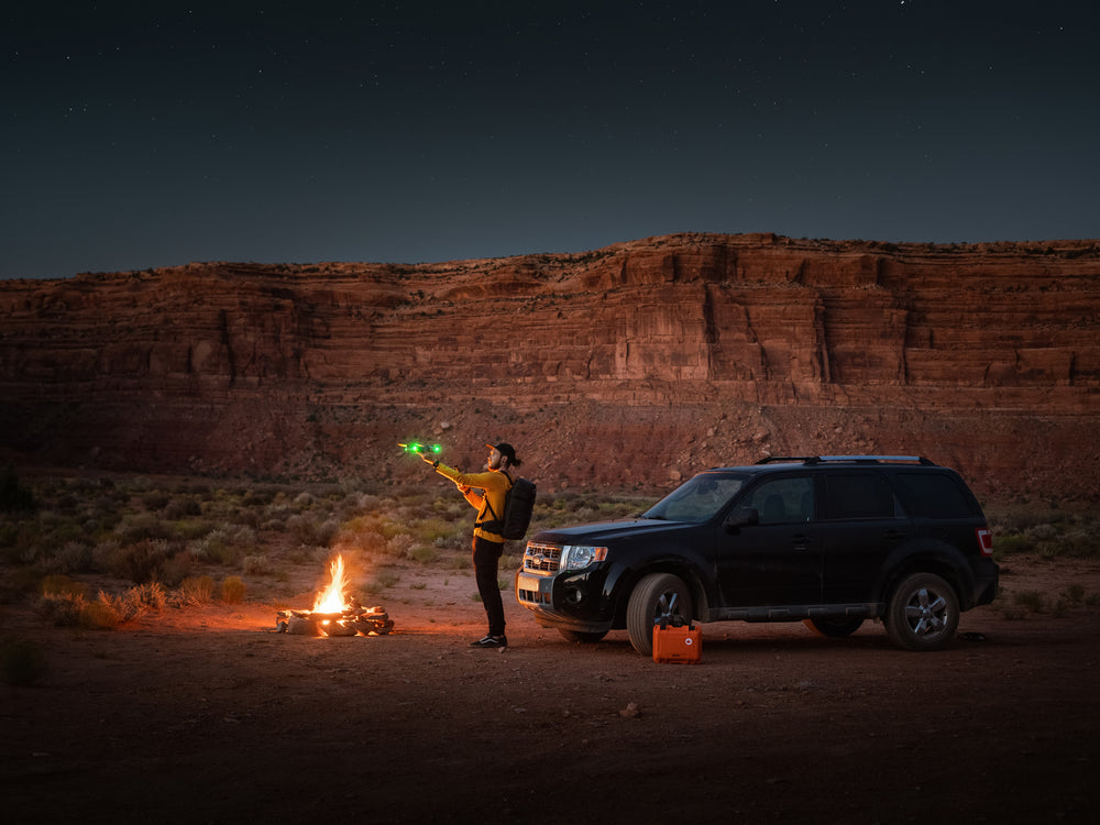 Person holding a green light in front of a car and campfire in a desert landscape at night.