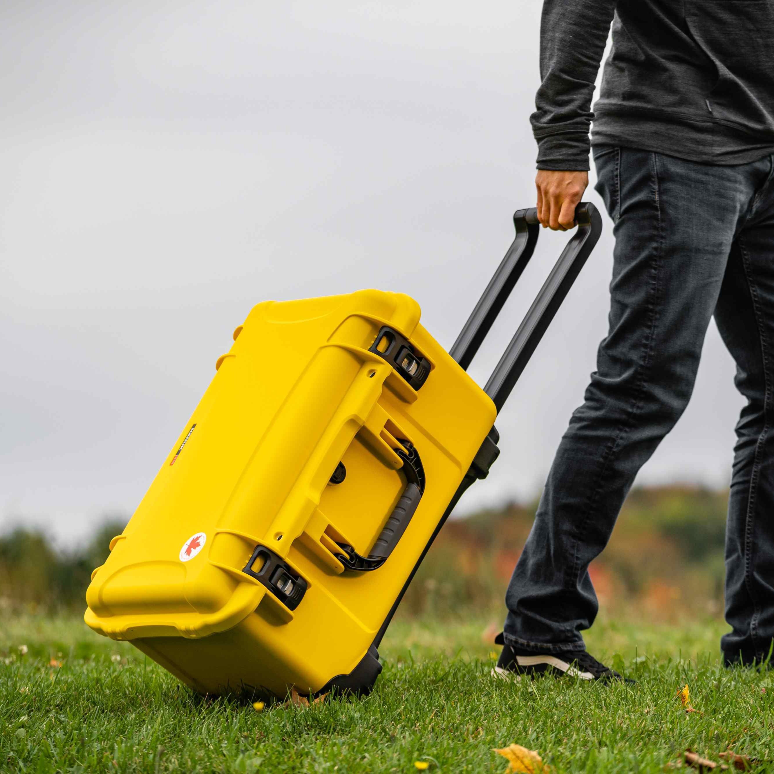 Person pulling a yellow suitcase on grass with a blurred background