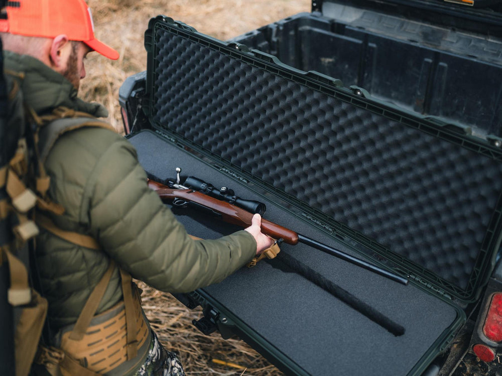 Person placing a rifle into a black hard-shell gun case outdoors.