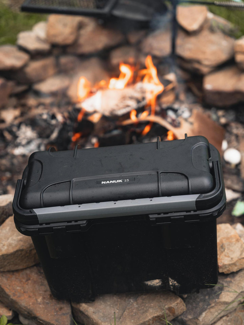 Black toolbox with 'Nanuk' branding on a stone surface near a campfire.