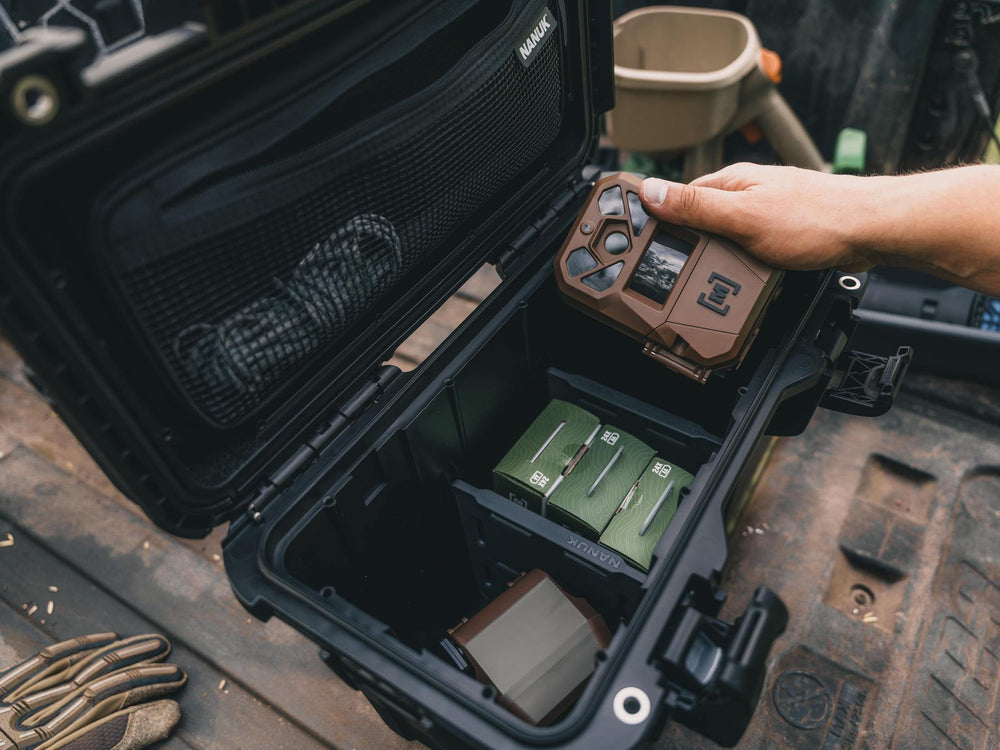 Person holding a device in an open black case with green items on a rugged surface