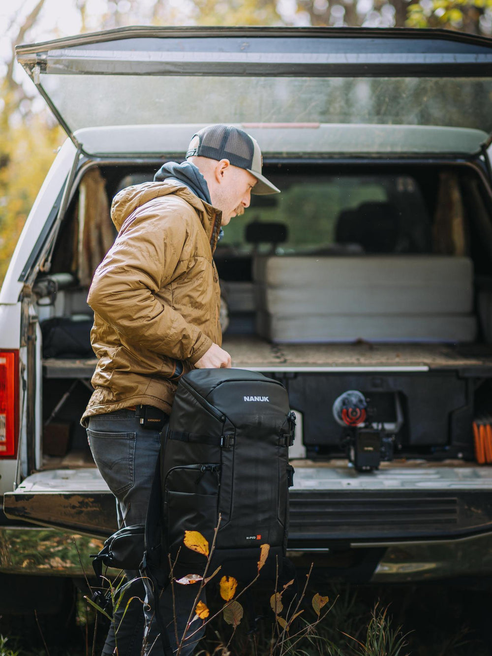 Man loading a large black bag into the back of an open truck in a natural setting.