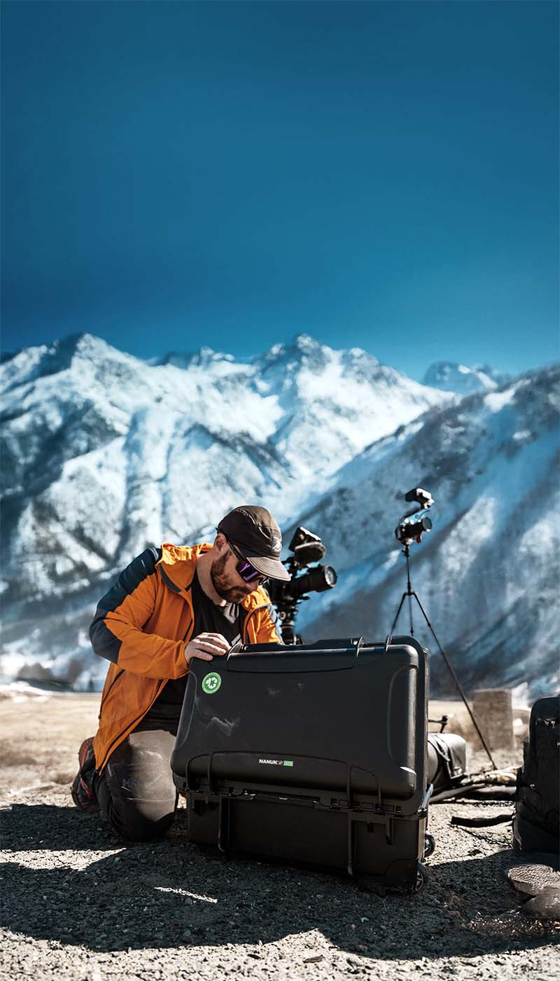 Men looking into his NANUK 935 Pro Photo Kit Hard Case in a winter environment with large mountains behind him.