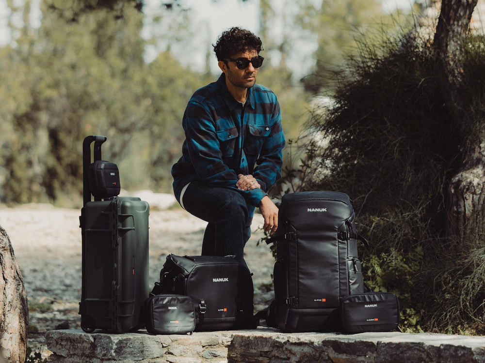 Man sitting outdoors with various camera bags and equipment