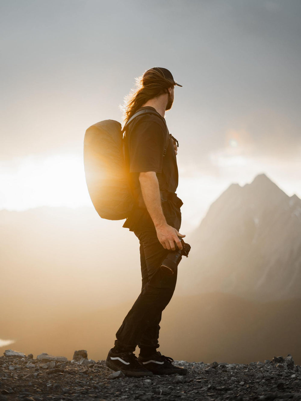 Person with a backpack standing on a mountain with a sunset or sunrise in the background