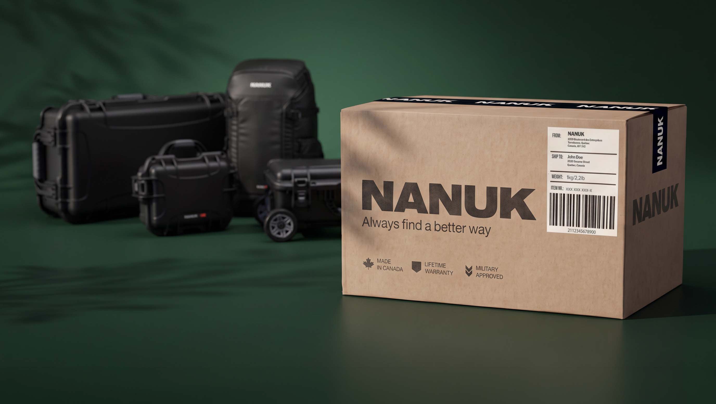A brown cardboard box with the brand name NANUK prominently printed on the front, shown in the foreground on a dark green studio background. Several black protective hard cases are arranged behind it.